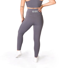 Load image into Gallery viewer, Back of a woman wearing full length grey leggings with the words Strong Girls Co. and a logo in the middle of the waistband and white training shoes
