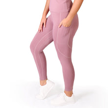 Load image into Gallery viewer, Side facing woman wearing full length pink activewear leggings with pockets with a small logo on the left side ankle, a matching pink crop top and white training shoes
