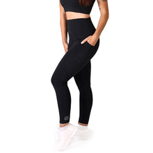 Load image into Gallery viewer, Side facing woman wearing full length black activewear leggings with pockets with a small logo on the left side ankle, a matching black crop top and white training shoes
