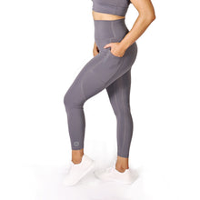 Load image into Gallery viewer, Side facing woman wearing full length grey activewear leggings with pockets with a small logo on the left side ankle, a matching grey crop top and white training shoes
