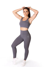 Load image into Gallery viewer, Front facing woman wearing full length grey activewear leggings with a small logo on the left hip below the waistband and a matching grey crop top showing their midriff and white training shoes
