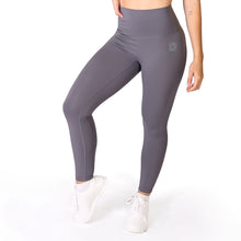 Load image into Gallery viewer, Front legs of a woman wearing full length grey activewear leggings with a small logo on the left hip below the waistband and white training shoes
