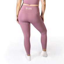 Load image into Gallery viewer, Back of a woman wearing full length pink leggings with the words Strong Girls Co. and a logo in the middle of the waistband and white training shoes
