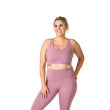 Load image into Gallery viewer, Front facing smiling woman wearing pink activewear leggings with a small logo on the front left hip below the waistband and a matching pink crop top with one hand on her hip and the other by her side. 
