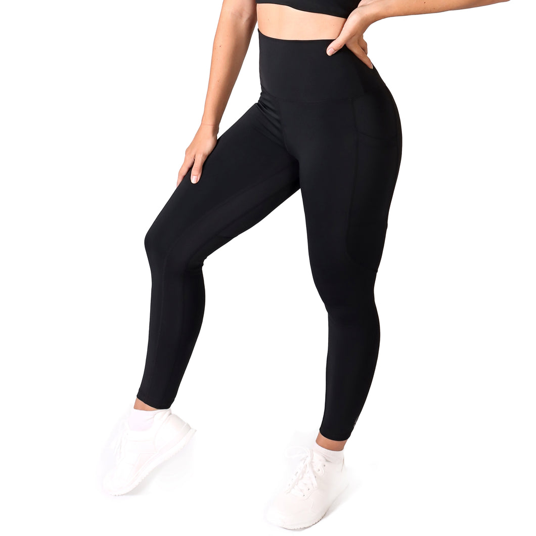 Side facing woman wearing full length black activewear leggings with pockets with a matching black crop top and white training shoes