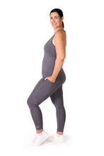 Load image into Gallery viewer, Side facing smiling woman, wearing full length grey activewear leggings with pockets with a small logo on the left side ankle, a matching grey top and white training shoes
