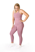 Load image into Gallery viewer, Front legs of a woman wearing full length pink activewear leggings with a small logo on the left hip below the waistband with a matching pink top and white training shoes

